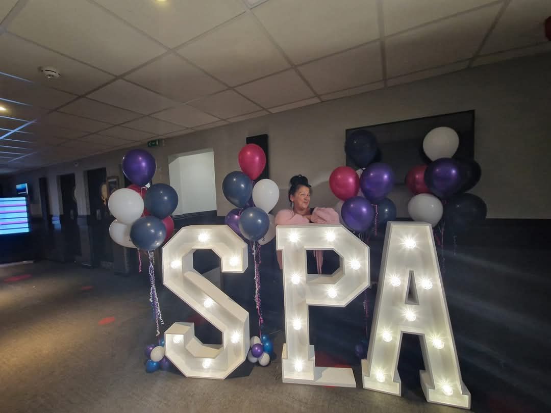 Light-up SPA letters and balloons in a corridor at the conference, with one of the team kneeling behind them