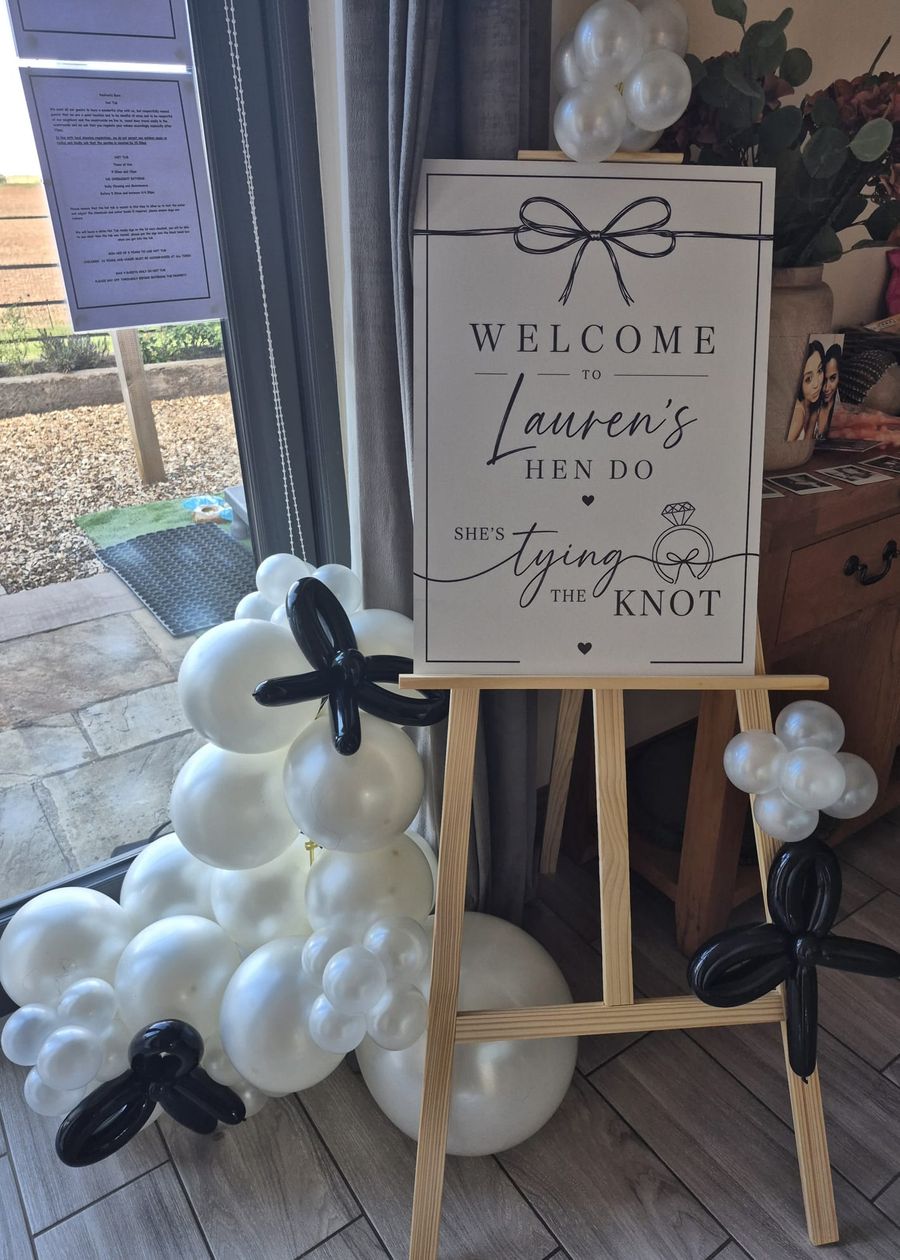 A welcome sign for a hen do on an easel, surrounded by white and black balloons