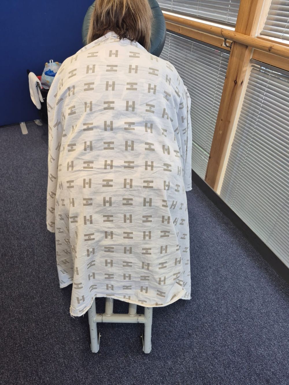 A member of staff seated in the massage chair, seen from behind, with a cream towel over their shoulders