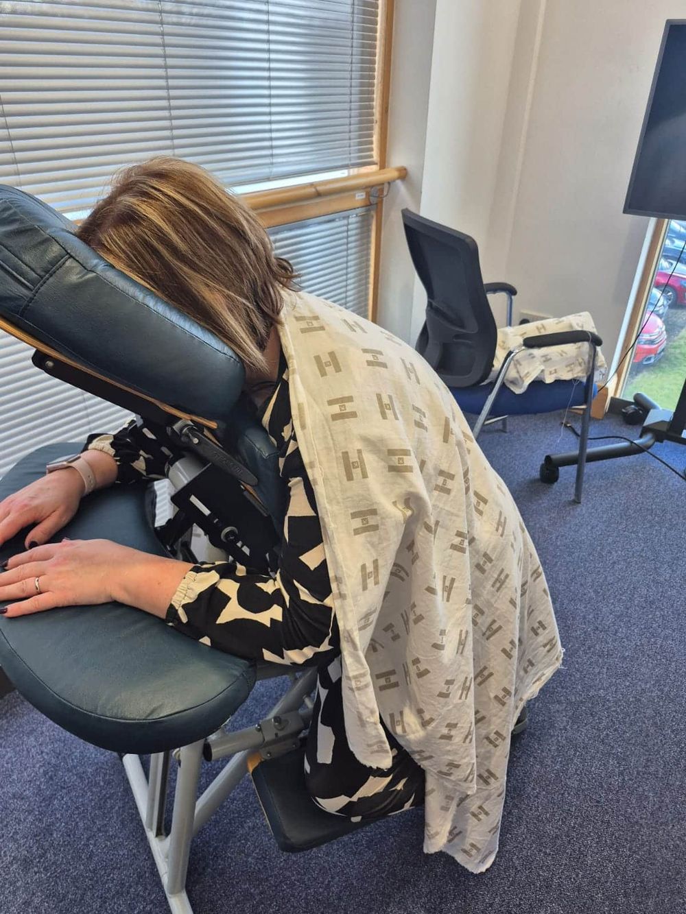 A member of staff leaning into the massage chair with a cream towel across their back, in a bright office